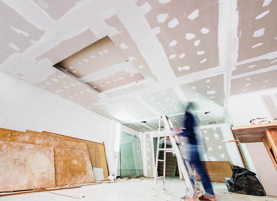 Drywall Contractor Insurance - Interior Work of a Large Room With Blurred View of a Carpenter Working on the Ceiling and Repairing Drywall